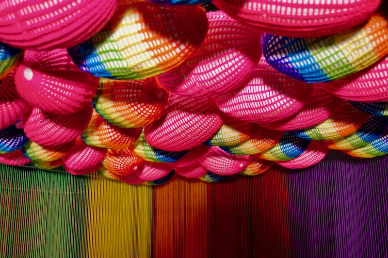 From the Wonder Art Gallery, this photo depicts balls of rainbow yarn hanging from the ceiling.